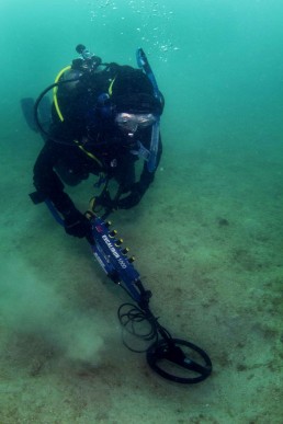 Diver undertakes a metal detector survey over a sandy area.